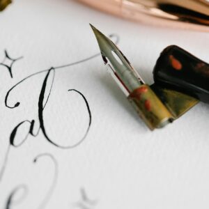 Close-up of artistic calligraphy with a fountain pen on white textured paper.